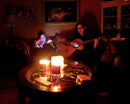 Couple sitting in a room with no power, one is playing the guitar and the female is reading a book